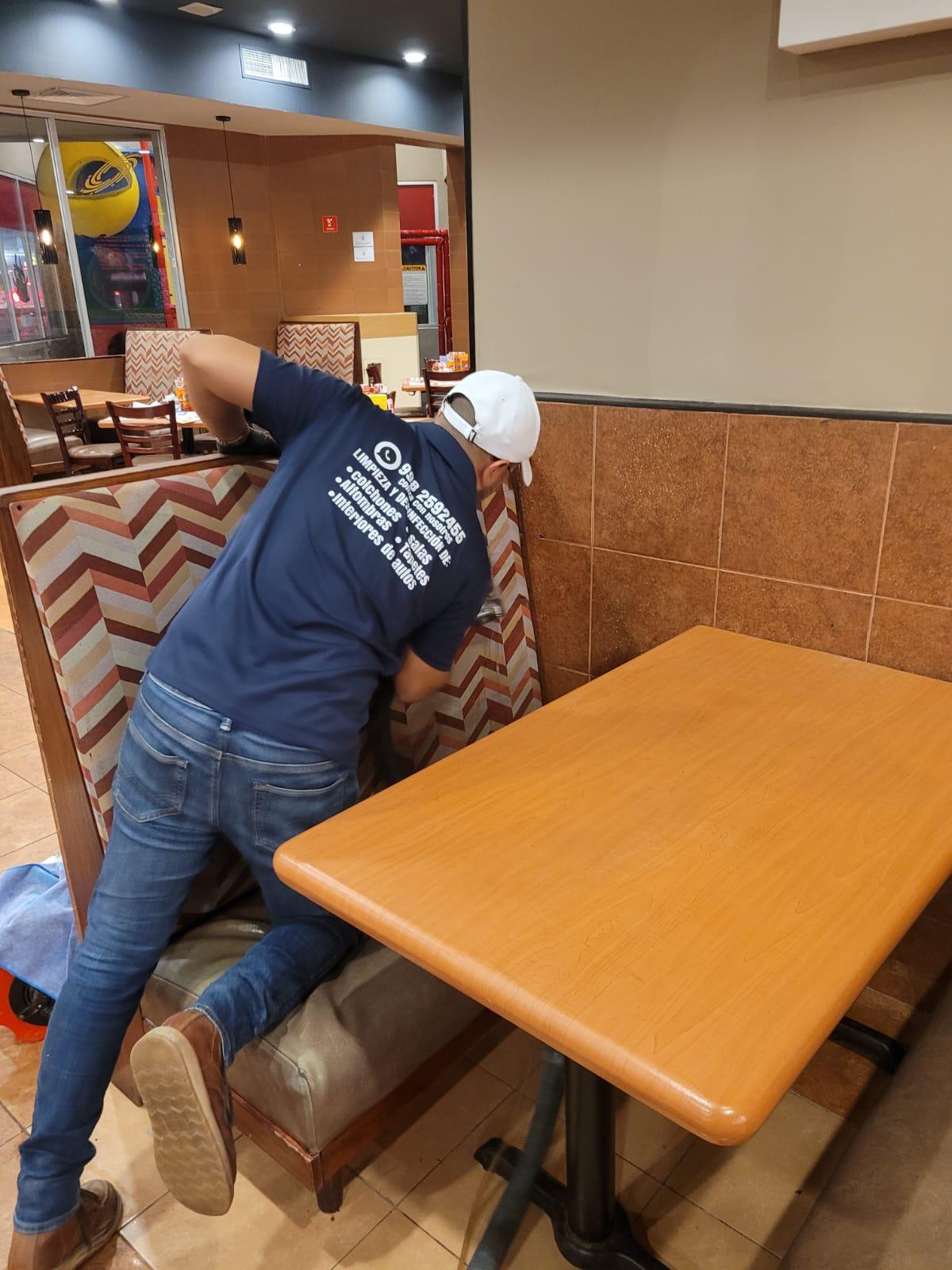 Persona limpiando un asiento de restaurante con respaldo de tela estampada.